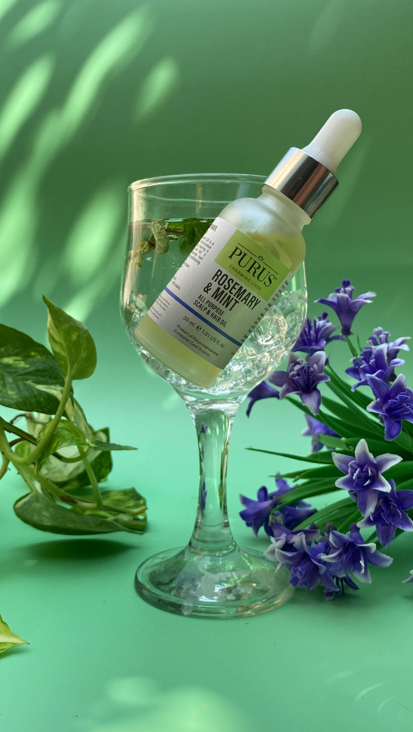 Elegant composition of rosemary and mint face serum in a wine glass with vibrant floral accents.